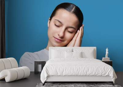 Young woman sleeping with closed eyes, on blue studio background Wall mural