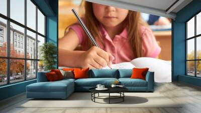 A little girl in a school class sits at a table and writes in a notebook Wall mural