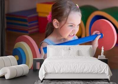 The child raises a heavy barbell in the gym. Wall mural