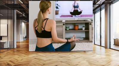 Pretty blonde woman doing yoga online at home infront TV. Stay home concept. Distance training concept Wall mural