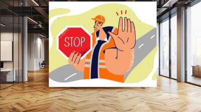 Man in builder uniform shows stop sign and makes caution gesture to warn drivers about road repairs Wall mural