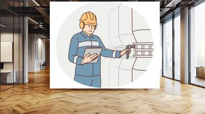 Man working at factory holds electronic tablet standing near industrial equipment and tanks Wall mural