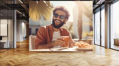 Smiling man holding glass of juice and sitting at cafe outdoors at summer Wall mural