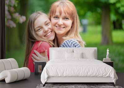 Happy family resting together - mother and daughter walking in park at summer or spring day. Beautiful woman hugs teen girl and smiling. Outdoors portrait - face to face. Wall mural