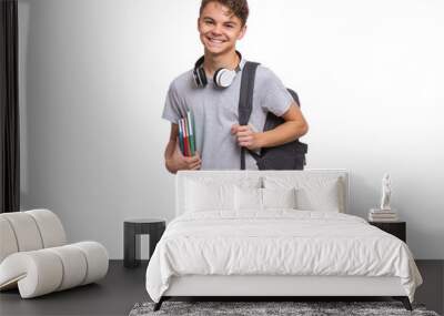 Happy teen boy with headphones and backpack holding books, isolated on white background. Smiling child looking at camera. Emotional portrait of handsome teenager guy Back to school. Wall mural