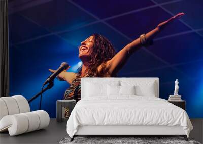 a female musician is viewed from a low angle as she sings and smiling with the audience with her hands raised up during a performance  Wall mural