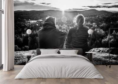 Cute couple sitting on the top of a mountain, facing the sun with flares between them, seen from behind, black and white Wall mural