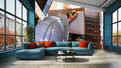 top view of construction inspector woman sits on the stairs during a home pre-purchase inspection, she uses clipboard to writes notes. with copy space Wall mural