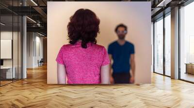 Woman standing far in front of a man. Woman seen from behind, standing in front of a blurry man in the background with some distance between them. Wall mural