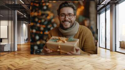 A young handsome man in a winter sweater against the background of a New Year's interior with a gift. New Year holidays concept. Christmas weekend and holidays. Boxing Day. Wall mural