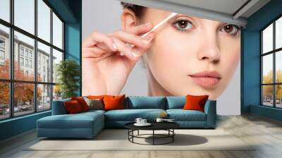 Beautiful face of a young  woman with a cotton stick in her hand, isolated.  Removing makeup with a cotton stick near eyes Wall mural