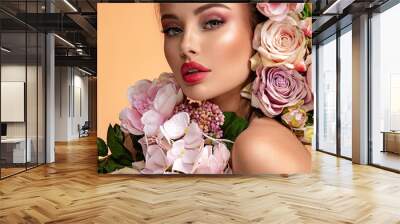 Beautiful white girl with flowers. Stunning brunette girl with big bouquet flowers of roses. Closeup face of young beautiful woman with a healthy clean skin. Pretty woman with bright makeup Wall mural