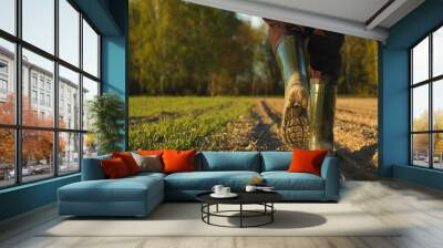 Close-up of a farmer's feet in rubber boots walking down a farmer field  dust rising from shoes. Low angle. One part is sown, the second part is not sown. Wall mural