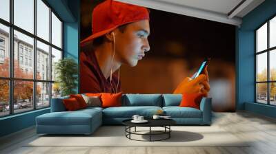 Close-up portrait of a young man with smartphone, on the city.   Teenage boy is using phone, outdoors.  Caucasian teenager in casual clothes with cell phone, urban scene. Soft focus effect. Wall mural