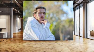 Close up portrait of handsome young man at the park in summer. Confident man looks to the camera, outdoor portrait. Calm face of a male model with brown hair. Guy with serious emotions looking camera Wall mural