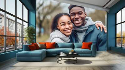 Happy young African couple in a park looking at the camera and smiling. Cheerful African couple standing and hugging each other in the city garden. Joyful couple outdoors on a spring day. Wall mural