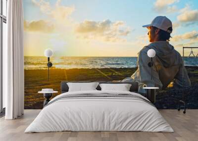 Man on a beach is looking distance during beautiful summer sunset. Human looks to the sun over horizon in the morning while sunrise. Happy person contemplates the beauty of nature. Freedom concept. Wall mural