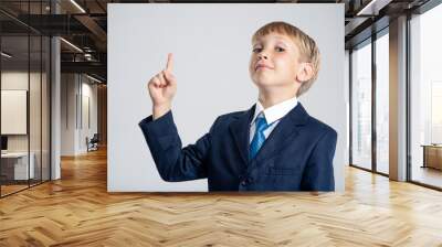 Photo of a  businessman  boy pointing finger up.  Portrait of white  kid in a blue business suit with an idea. 8 years old child dressed in a business formal suit with tie with an idea. Wall mural