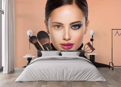 Portrait of a girl with  tools for making makeup near face.  One half face of a beautiful white woman with  bright makeup. Woman holds makeup brush and eyelash curler.  Wall mural