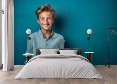 Portrait of a smiling teen boy in a blue shirt on a blue background.  Happy Teen boy in blue shirt smiling on blue background. Cheerful blonde  kid looks to the camera. Digital art Wall mural