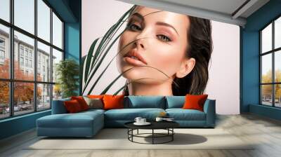 Young beautiful woman with green leaves near face and body. Skin care beauty treatments concept.  Closeup girl's face with green leave. White model with clean, health skin of face - posing at studio Wall mural