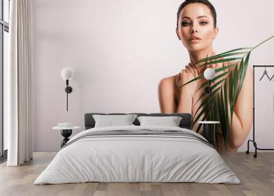 Young beautiful woman with green leaves near naked body. Body care beauty treatments concept.  Girl's  face with green flowers. Wall mural