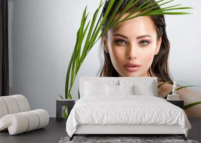 Young beautiful woman with healthy skin of face and palm leaves. Closeup fresh face of an attractive caucasian girl with green plants. Model with bright brown eye makeup. Skin care concept. Wall mural