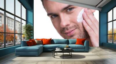 Young handsome man applying cream. Wall mural