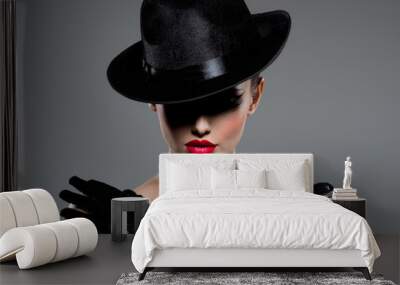 Сlose-up portrait of a woman in a black hat and gloves with red lips Wall mural