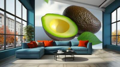 A photo of a green avocado cut in half with a brown pit. The avocado is sitting on a white table with a white background. Wall mural