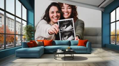 Happy gay lesbian couple holding ultrasound photo scan at home. Lgbt surrogate pregnancy concept Wall mural