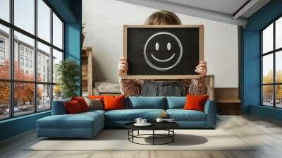 A young girl holds a chalkboard with a smiley face drawn on it Wall mural