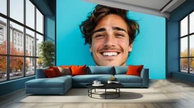 Smiling young man with wavy hair against a blue background. Ideal for health, happiness, and lifestyle concepts in stock photography. Wall mural