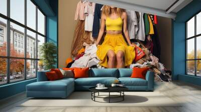 Woman wearing yellow outfit sitting on a massive stack of assorted clothes, showcasing the overwhelming extent of consumerism and its impact on individuals and the environment Wall mural