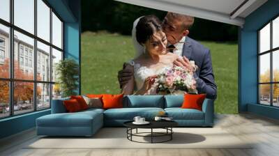 A bride and groom are standing in a field, with the bride holding a bouquet and the groom holding her hand Wall mural