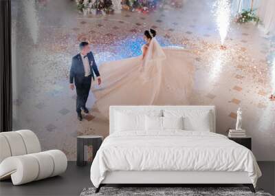 A bride and groom are walking down a dance floor with fireworks in the background. The bride is wearing a long white dress and the groom is wearing a suit. Scene is celebratory and romantic Wall mural