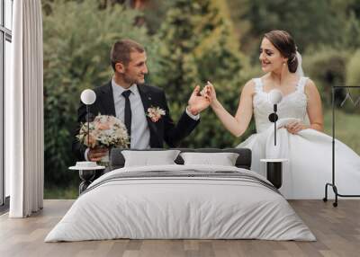 A bride and groom are walking down a path, the bride is holding a bouquet. The bride is wearing a white dress and the groom is wearing a black suit Wall mural