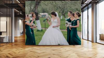 A bride and her bridesmaids are posing for a picture in a field. The bride is wearing a white dress and holding a microphone. The bridesmaids are all wearing green dresses and holding flowers Wall mural