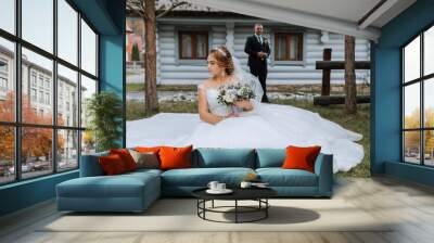 A bride sits in a field with a bouquet of flowers. A groom stands behind her. The scene is a wedding Wall mural