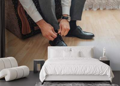 A man is putting on his shoes. He is wearing a watch and is sitting on a chair Wall mural