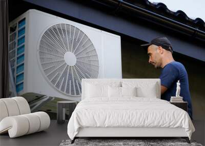 A man is working on an air conditioner. He is wearing a blue shirt and a hat Wall mural