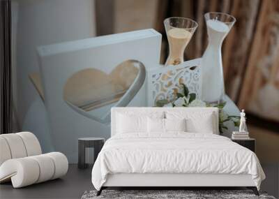 A white table with a heart-shaped frame, a vase of flowers, and two sand timers. The heart-shaped frame is placed in the center of the table Wall mural