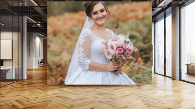 A woman in a white dress is holding a bouquet of pink flowers. She is smiling and she is happy. Concept of joy and celebration, likely representing a wedding or a special occasion Wall mural