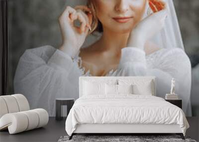 A woman in a white dress is wearing a veil and earrings. She is smiling and looking at the camera Wall mural