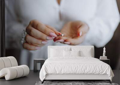 A woman is holding a ring in her hand. The ring is a diamond and is set in a gold band. The woman is wearing a white dress and has her nails painted. Concept of elegance and sophistication Wall mural