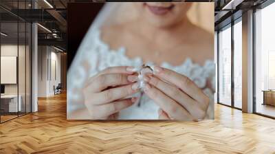 A woman is holding a ring in her hand. The ring is gold and has a diamond on it. She is wearing a white wedding dress Wall mural