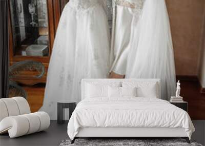 A woman is standing in front of two white wedding dresses, one of which is a long gown Wall mural