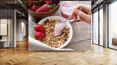 Healthy breakfast. Muesli and yogurt with strawberries. A woman's hand puts a spoonful of yogurt in the muesli Wall mural