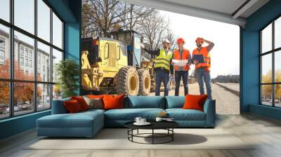 male workers engineers in helmets talking near the bulldozer and excavator Wall mural