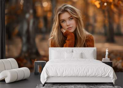 Young woman in orange sweater sitting outdoors with autumn foliage background Wall mural